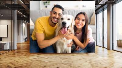 Portrait of smiling diverse couple hugging their pet dog, smiling at camera, indoors Wall mural