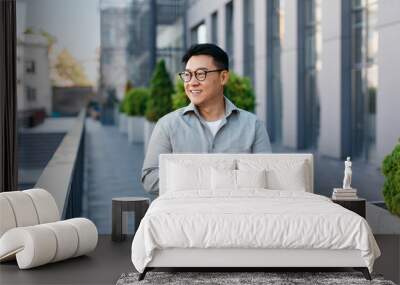 Positive asian middle aged male entrepreneur checking emails on smartphone while walking by business center Wall mural