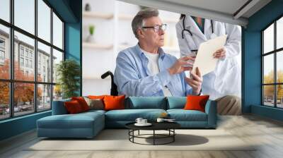 Positive female doctor offering disabled elderly man to sign insurance contract at home Wall mural