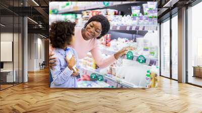 Positive young black mom teaching her daughter how to choose dairy products at grocery store Wall mural