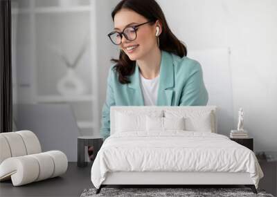 Positive young caucasian business woman in suit, glasses with computer work, enjoys professional occupation Wall mural