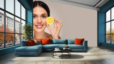 Positive young caucasian lady with perfect face, show yellow lemons fruits, isolated on gray studio background. Vitamin C recommendation, beauty and skin care, rejuvenating, copy space Wall mural