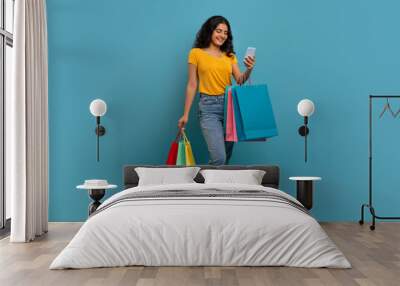 Positive young indian woman with purchases and smartphone Wall mural