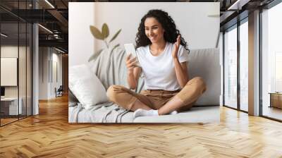 Positive young woman sitting on couch, having online call Wall mural