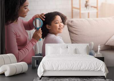 Pregnant afro woman brushing her cute little daughter's hair at home Wall mural