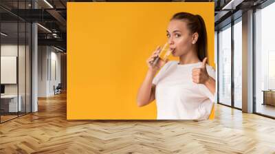 Pretty girl drinking water from glass and gesturing thumb up Wall mural