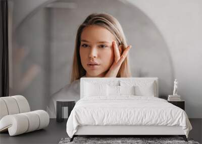 Pretty young woman looking at mirror and touching face while doing morning beauty routine in bathroom Wall mural