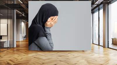 Profile portrait of crying muslim woman covering her face with hands Wall mural