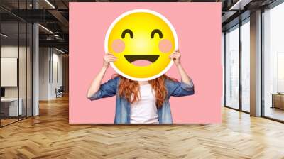 Redhead girl hiding her face behind happy emoji smile Wall mural