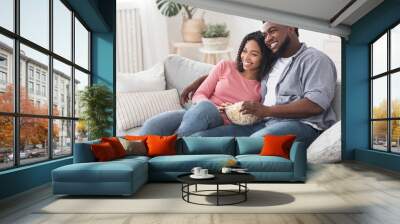 Relaxed african american couple watching tv, sitting on couch with popcorn Wall mural