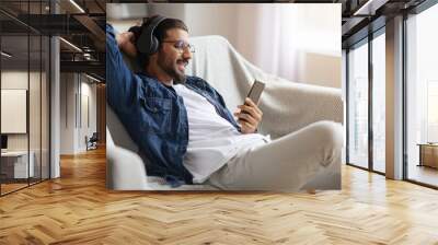 Relaxed indian guy enjoying listening music on smartphone with wireless headphones Wall mural