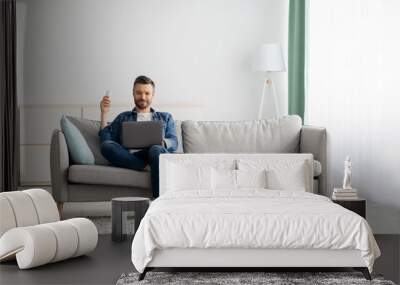 Relaxed man with laptop sitting on couch at home Wall mural