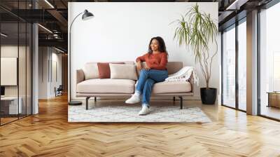 Relaxing Afternoon at Home: Smiling Black Woman on Sofa in Living Room Wall mural