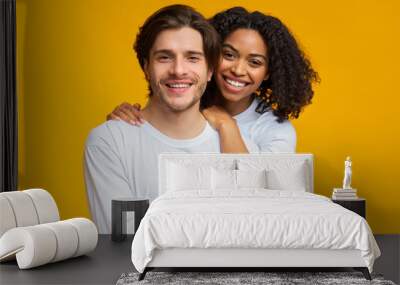 Romantic interracial couple embracing and posing over yellow background Wall mural