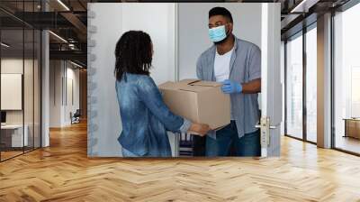 Safe Delivery Service. Black courier wearing mask giving cardboard box to woman Wall mural