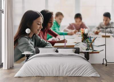 Schoolgirl Writing Essay During Class With Mixed Children In Classroom Wall mural