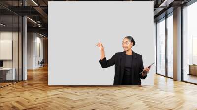 Smiling African American businesswoman in professional attire holding a tablet while pointing upwards Wall mural