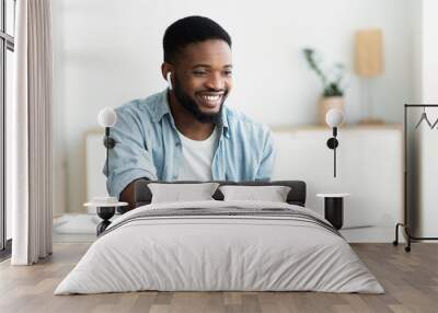 Smiling african-american guy in earphones studying foreign language online Wall mural