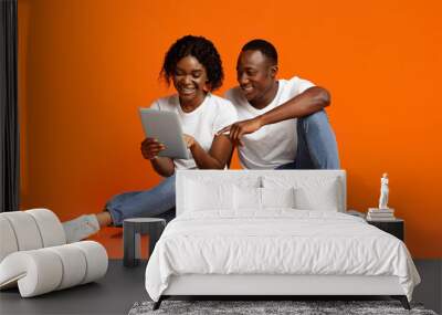 Smiling african american lovers using digital tablet over orange Wall mural