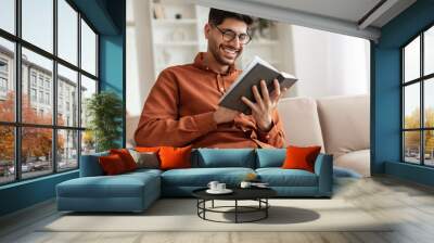 Smiling Arab man in glasses reading book Wall mural