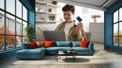 Smiling asian guy showing credit card at home Wall mural