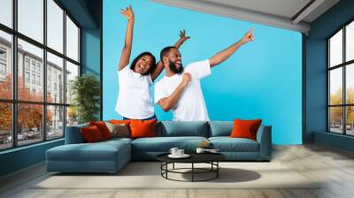 Smiling black couple celebrating win, pointing aside at copy space Wall mural