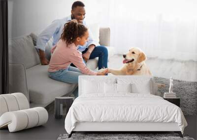 Smiling black girl playing with dog in the living room Wall mural