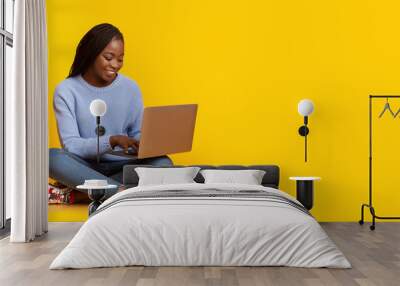 Smiling black girl using laptop over yellow background Wall mural