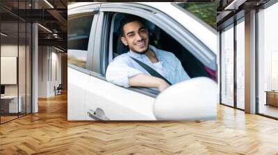 Smiling cheerful millennial arab man fastened with belt enjoy travel on new car and look out the open window Wall mural