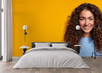 Smiling curly-haired woman on yellow background, panorama, copy space Wall mural