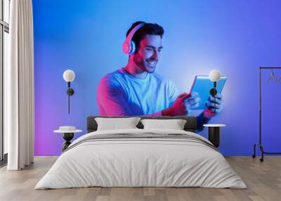 Smiling guy in headphones plays at tablet Wall mural