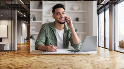 Smiling handsome millennial islamic guy manager with beard speaks by phone at workplace with laptop in home Wall mural