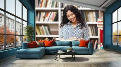 Smiling latina woman reading a book at library Wall mural