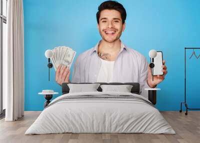 Smiling man showing blank phone screen, holding bunch of money Wall mural