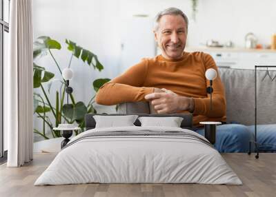 Smiling mature man sitting on the couch and posing Wall mural