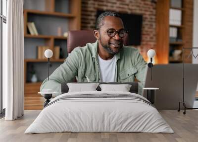 Smiling middle aged african american male in glasses and casual working on laptop in home office interior Wall mural