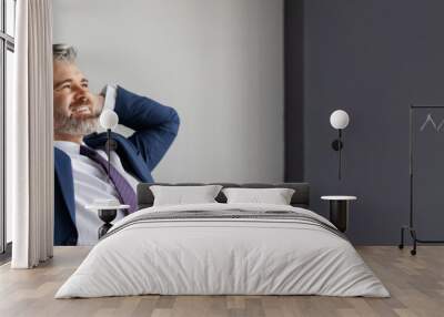 Smiling middle aged businessman leaning back in chair at workplace in office, handsome happy entrepreneur in suit sitting at desk with hands behind head, resting after successful day, copy space Wall mural