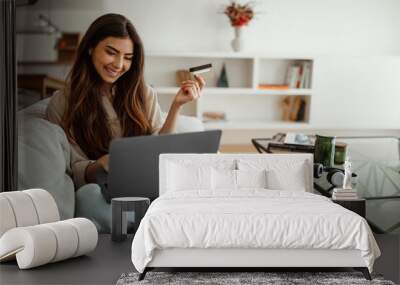 Smiling millennial mixed race woman shopaholic typing on laptop, using credit card, enjoy online shopping Wall mural