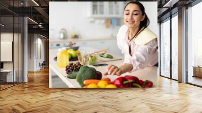 Smiling woman cooking salad, grabbing vegetables from table Wall mural