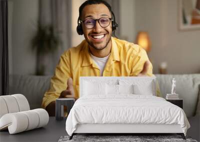 Smiling young African American man in headset chatting online, having webinar or video conference at home office Wall mural