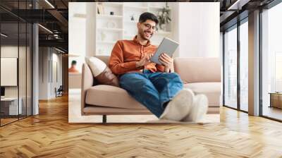 Smiling young Arab man using digital tablet at home Wall mural