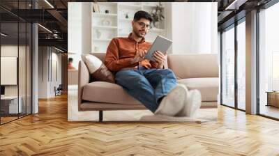 Smiling young Arab man using digital tablet at home Wall mural