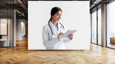 Smiling young hindu woman doctor in white coat work on tablet, isolated on white background Wall mural