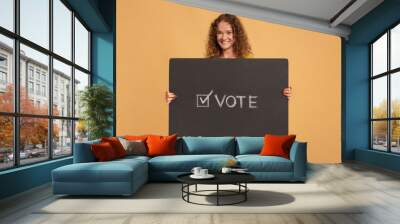 Smiling young redhead curly female holding holding vote sign, poster or banner with inscription Wall mural