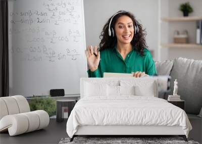 Smiling young woman teaching maths to students online, waving hello Wall mural