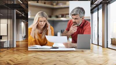 Stressed husband and wife sitting at kitchen table, reading documents Wall mural