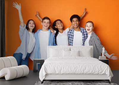 Students having fun over orange studio background Wall mural