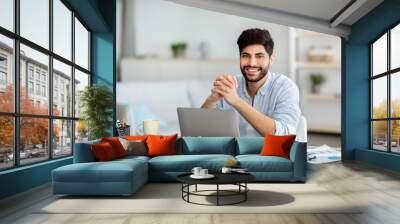 Successful freelancer. Happy arab man sitting at desk with laptop and smiling to camera Wall mural