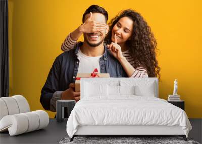 Surprise Present. Romantic young arab woman covering boyfriend's eyes and giving gift Wall mural