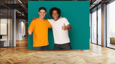 Teenage friends showing thumbs up over blue background Wall mural